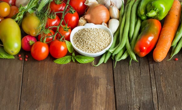Quinoa in a bowl and fresh vegetables on a wooden table