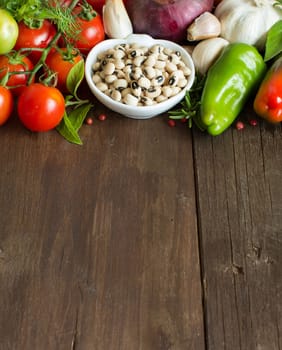 Black eyed peas in a bowl and vegetables on wood