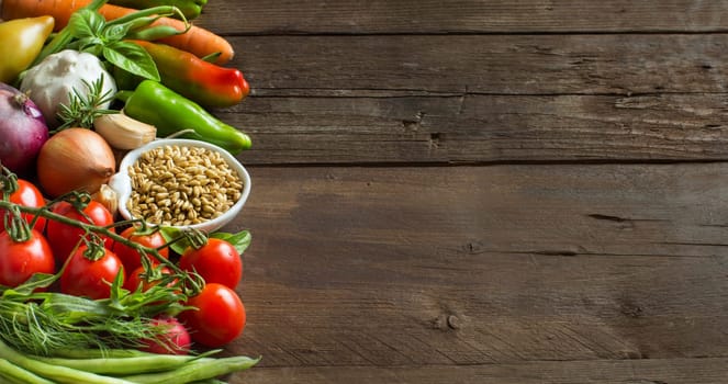 Spelt in a bowl and fresh vegetables on a wooden table