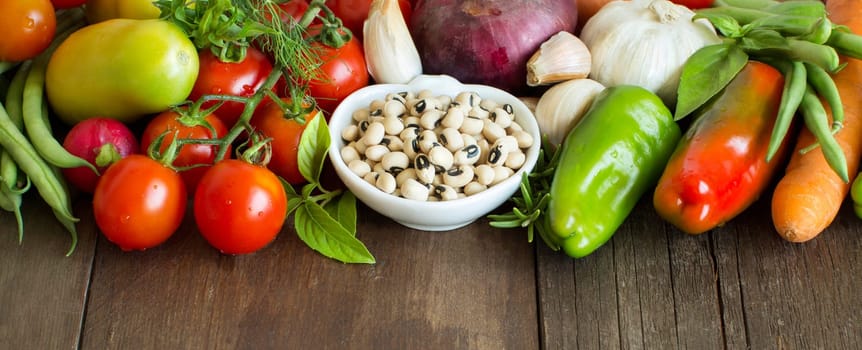 Black eyed peas in a bowl and vegetables on wood