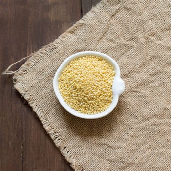 Raw millet in a bowl on burlap and wood