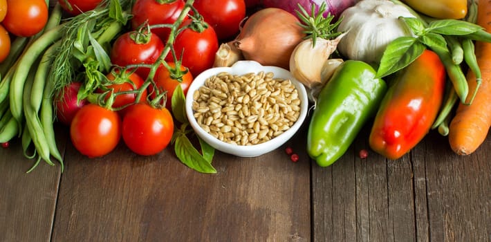 Spelt in a bowl and fresh vegetables on a wooden table