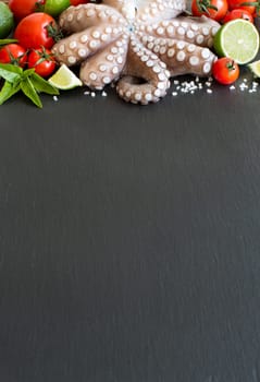 Raw octopus with lime, tomatoes and basil over dark background