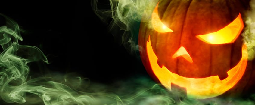Jack o lantern with evil glowing eyes emanating green smoke,on black panoramic background with copyspace