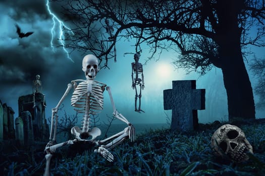 Nighttime Halloween scene with skeletons at a cemetery and the silhouette of a dead tree in the blue moonlight