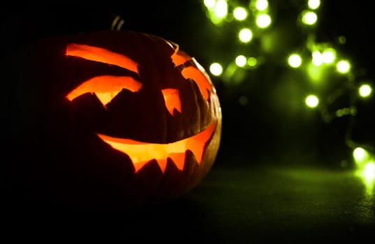 carved face of pumpkin glowing on halloween on green bokeh light background