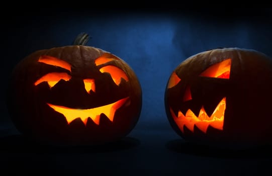 two carved faces of pumpkins glowing on halloween on blue background