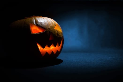 the carved face of pumpkin glowing on halloween on blue background