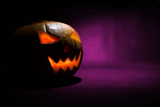 the carved face of pumpkin glowing on halloween on purple background