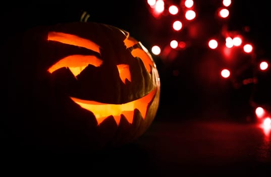 carved face of pumpkin glowing on halloween on red light background bokeh