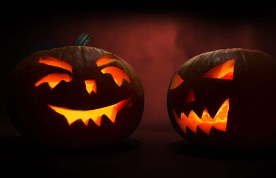 two carved faces of pumpkins glowing on halloween on red background