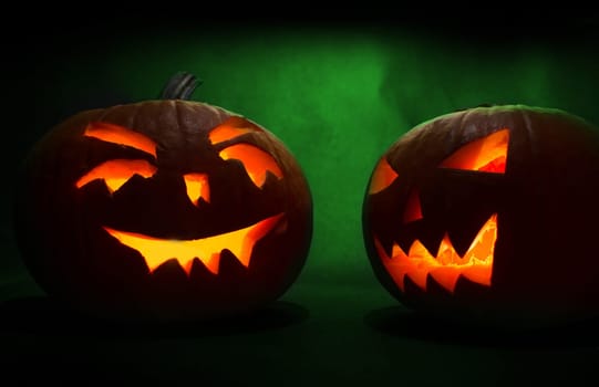 two carved faces of pumpkins glowing on halloween on green background