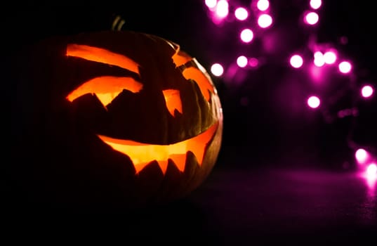 carved face of pumpkin glowing on halloween on purple bokeh light background