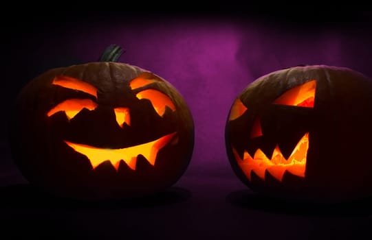 two carved faces of pumpkins glowing on halloween on purple background