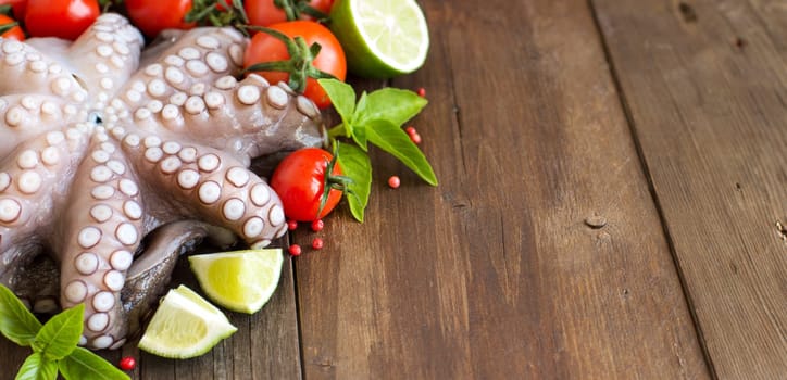 Raw octopus with lime, tomatoes and basil over wooden background