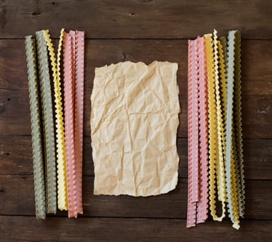 Tricolor mafalde pasta and paper on the old wooded table