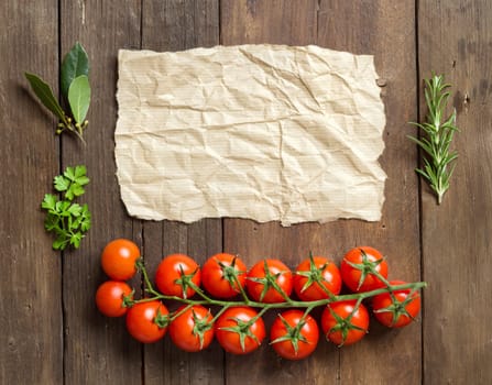 Cherry tomatoes, herbs and craft paper on wooden background