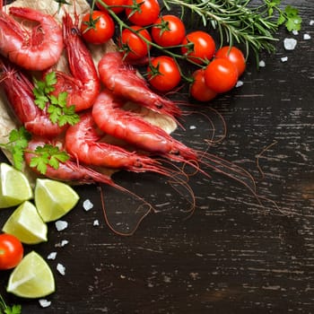 Raw shrimps with tomatoes, lime and herbs over dark background