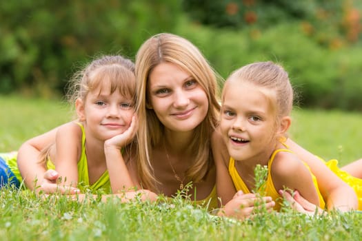 Mother and two daughters lie on the green grass, and looked into the frame