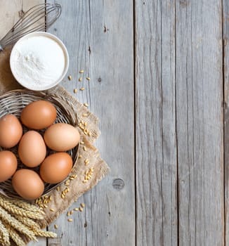 Chicken eggs, whisk, wheat and flour on the old wood