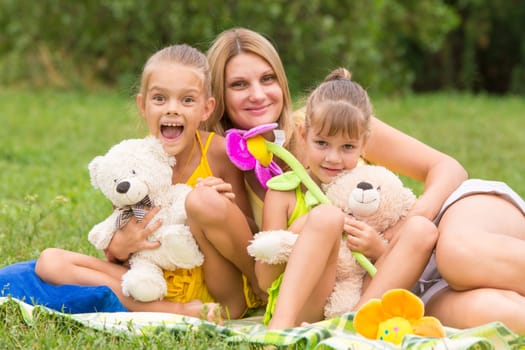 Mother and two daughters sitting with soft toys on a picnic