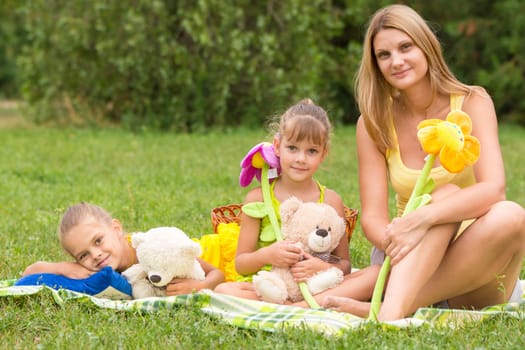 Mother and daughter sitting with soft toys on a picnic and watch the shot