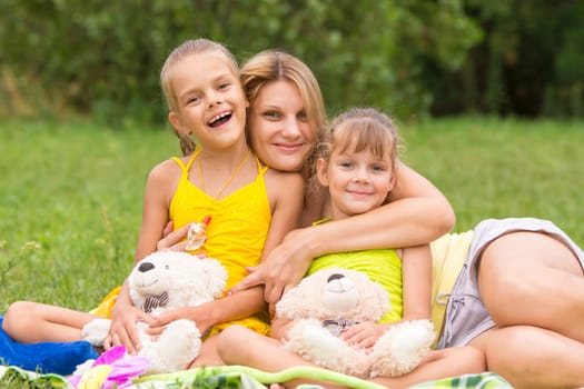Young mother on a picnic hugging two daughters, five and seven years
