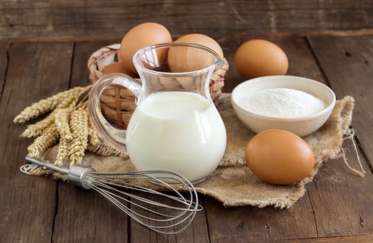 Milk, flour, wheat, whisk and eggs on the old wooden table