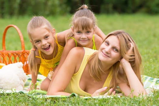 Mother and two daughters lie on each other on the green grass