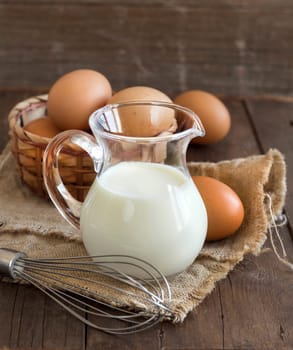 Milk, whisk and eggs on the old wooden table