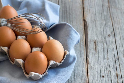 Chicken eggs in the box and whisk on the blue napkin