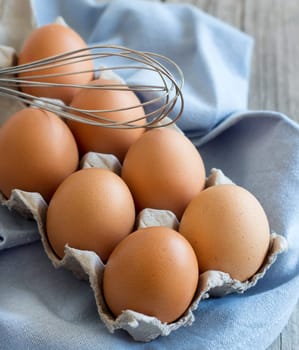 Chicken eggs in the box and whisk on the blue napkin