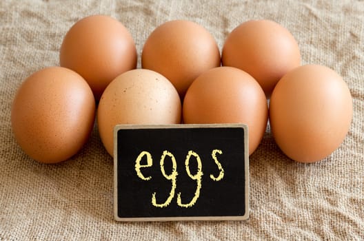 Chicken eggs and small chalkboard on burlap close up