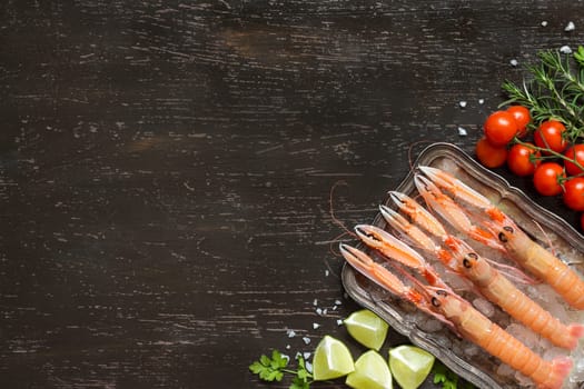 Raw langoustines on ice with lime,tomatoes and herbs over dark background