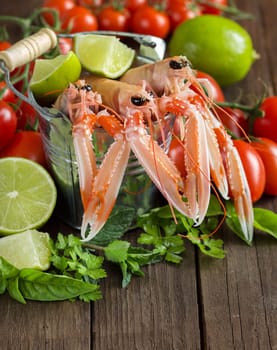 Raw langoustine in a bucket with vegetables and herbs on wood