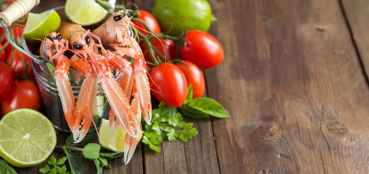 Raw langoustine in a bucket with vegetables and herbs on wood