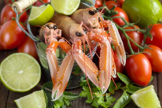 Raw langoustine in a bucket with vegetables and herbs on wood