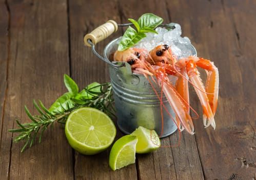 Raw langoustine in a bucket with vegetables and herbs on wood