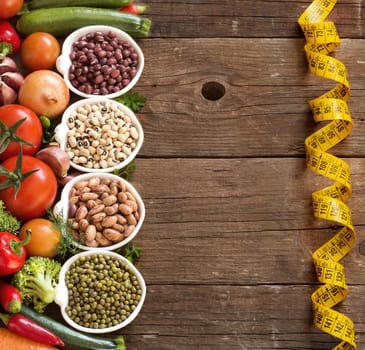 Legumes in bowls and vegetables on a wooden table
