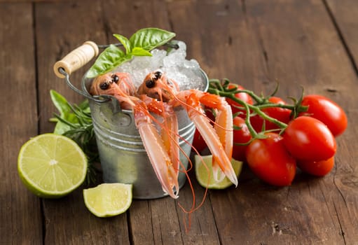 Raw langoustine in a bucket with vegetables and herbs on wood