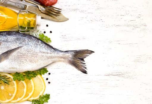 Fresh dorado fish, lemon, olive oil and vintage fork and knife on wooden board