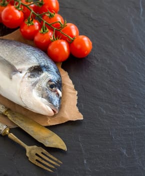 Fresh dorado fish, silver fork and knife and tomatoes