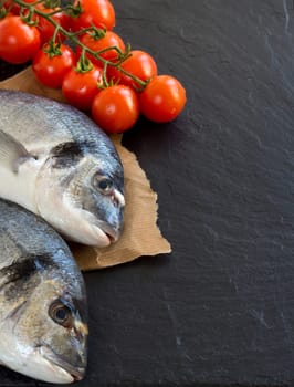 Fresh dorado fish and tomatoes on dark vintage background