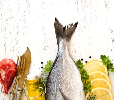Fresh dorado fish, lemon, olive oil and vintage fork and knife on wooden board
