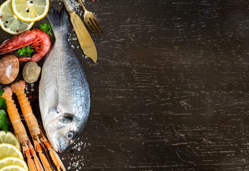 Fresh dorado fish, seafood and vegetables on a dark background