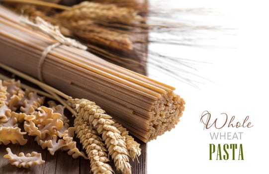 Whole wheat italian pasta with wheat spikes on wood