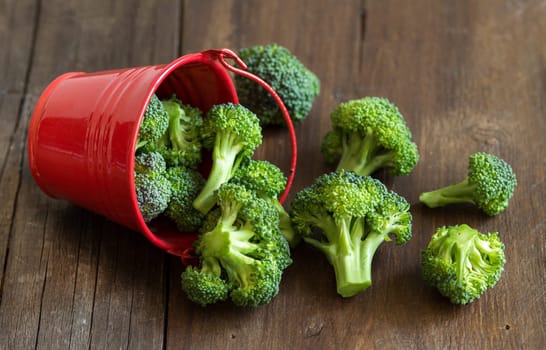 Green broccoli in red bucket on old wood