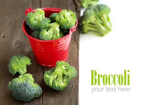 Green broccoli in red bucket on old wood
