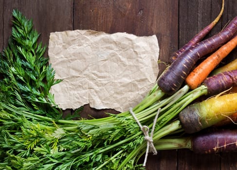 Fresh organic rainbow carrots and craft paper on wood