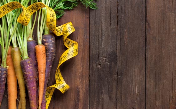 Fresh organic rainbow carrots and yellow measuring type on wood